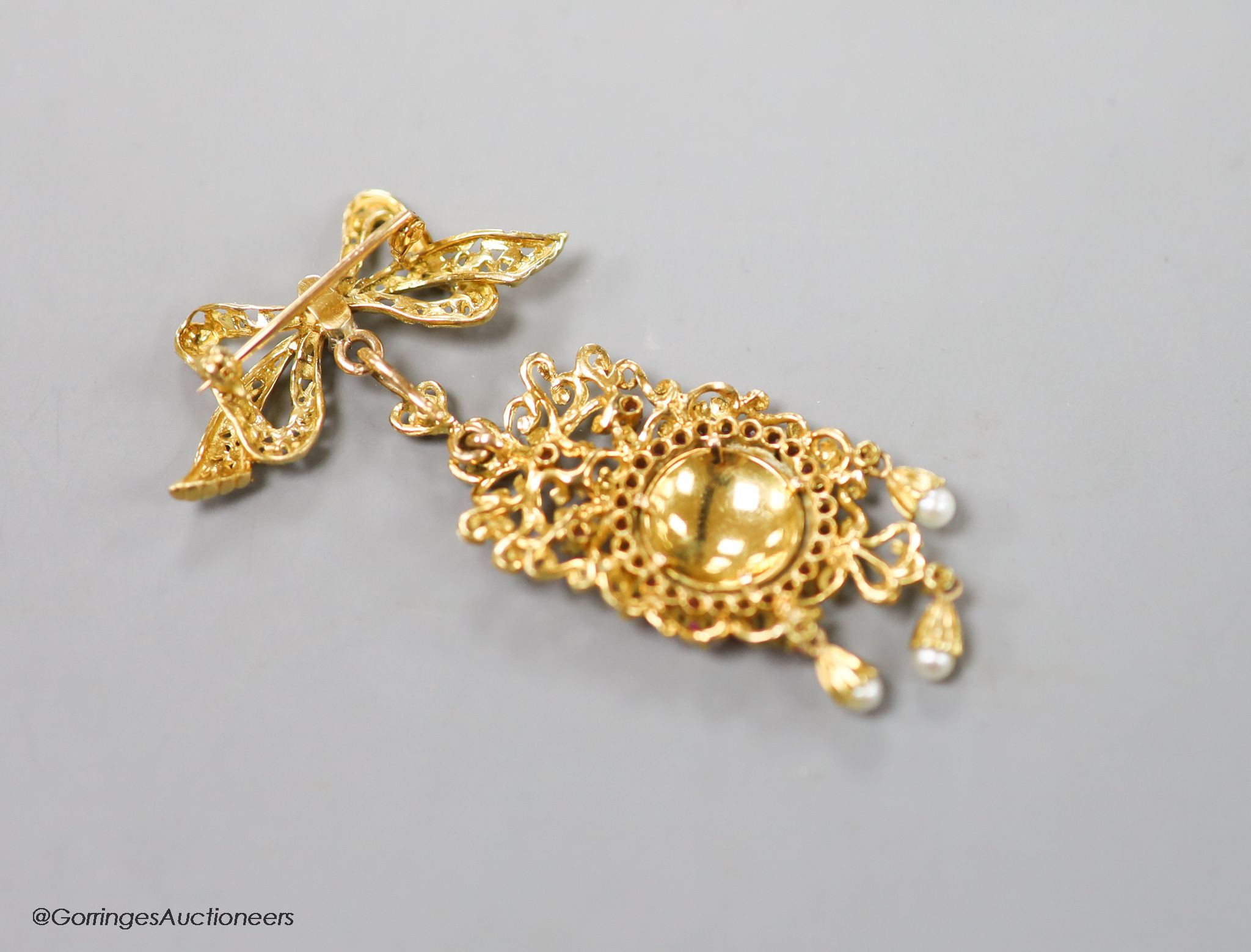 An early 1960's 18ct gold, ruby seed pearl and enamel set drop pendant, suspended from a ribbon bow brooch, import marks for Birmingham, 1960, overall 65mm